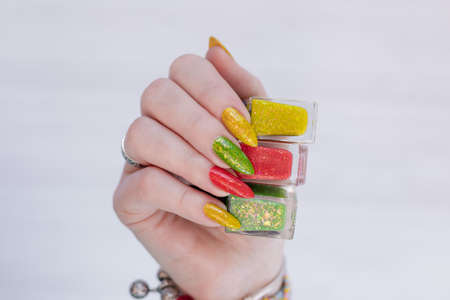 Female hand with long nails and multi-colored manicure, bottles of nail polishes