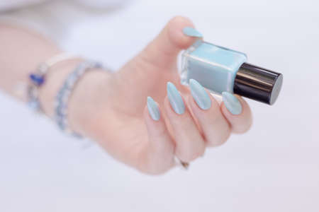 Female hand with long nails and light blue manicure with bottles of nail polishの写真素材