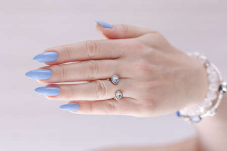 Female hand with long nails and light blue manicure with bottles of nail polish