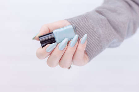 Female hand with long nails and light blue manicure with bottles of nail polish