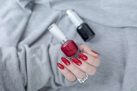 Female hand with long nails and a bottle bright red color nail polishの写真素材