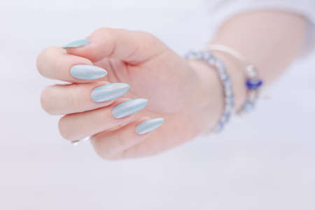 Female hand with long nails and light blue manicure with bottles of nail polishの写真素材