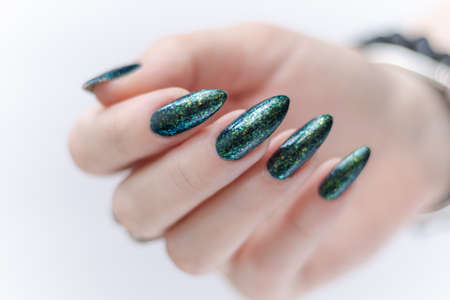 Female hand with long nails and a bottle of dark emerald green nail polish
