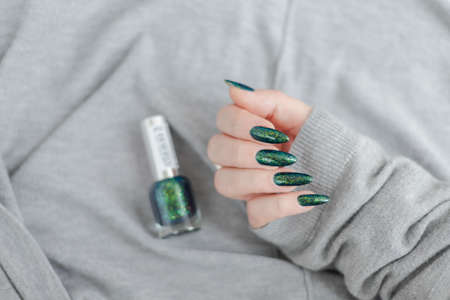 Female hand with long nails and a bottle of dark emerald green nail polish
