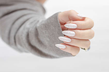 beautiful woman hands with long nails light white manicure and a bottle of nail polishの写真素材