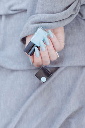 Female hand with long nails and light blue manicure with bottles of nail polishの写真素材