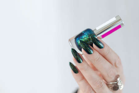Female hand with long nails and a bottle of dark emerald green nail polish