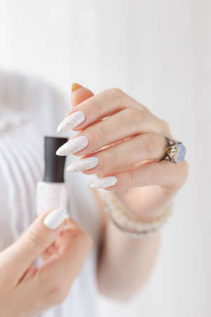 beautiful woman hands with long nails light white manicure and a bottle of nail polish