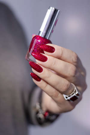 Female hand with long nails and a bottle bright red color nail polish