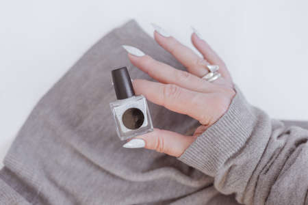 beautiful woman hands with long nails light white manicure and a bottle of nail polishの写真素材
