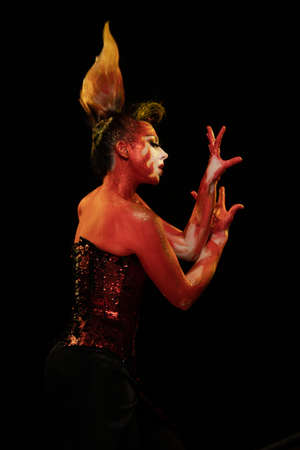 Young woman dancing in the image of Flames and Fire in a red body art emotionally posing on a black...