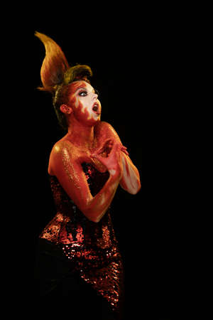 Young woman dancing in the image of Flames and Fire in a red body art emotionally posing on a black backgroundの写真素材