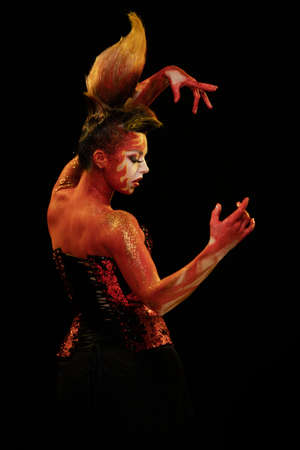 Young woman dancing in the image of Flames and Fire in a red body art emotionally posing on a black...