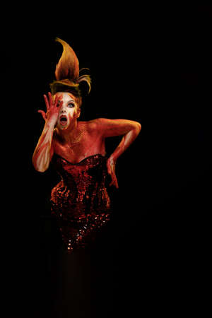 Young woman dancing in the image of Flames and Fire in a red body art emotionally posing on a black backgroundの写真素材