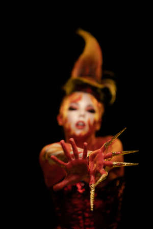 Young woman dancing in the image of Flames and Fire in a red body art emotionally posing on a black...