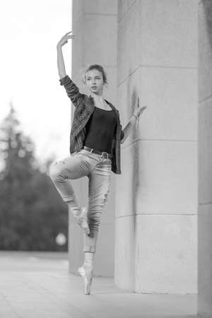 Black and white photo of a ballerina girl in jeans and pointe shoes, dancing and posing in the city on the streetの写真素材