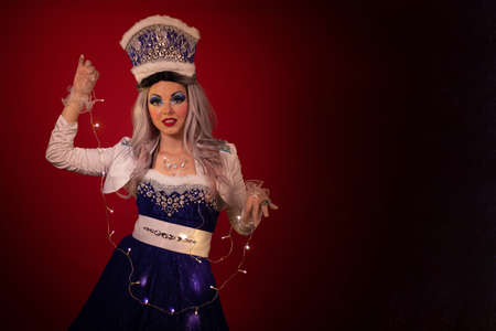 Snow Maiden in an elegant furry blue suit with a crown on her head and a garland in her hands posing...