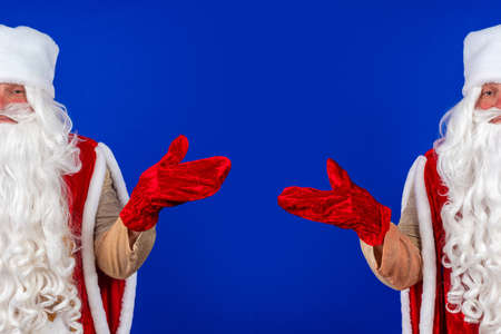 Emotional Santa Claus with a long white beard in a red coat and white hat posing on a blue backgroundの写真素材