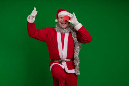 Emotional male actor in a costume of Santa Claus holds a small red gift box in his hands and poses...