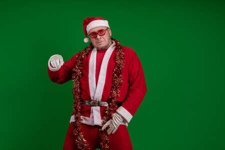 Male actor in a costume of Santa Claus in large pink glasses and with a red garland of tinsel in his...