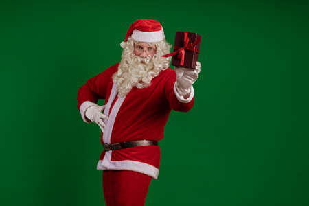 Emotional male actor in a costume of Santa Claus holds one gift box in his hands and poses on a...