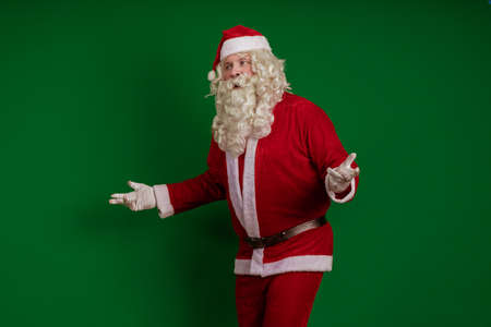 Emotional male actor in a costume of Santa Claus with a long beard gestures and poses on a green chrome backgroundの写真素材