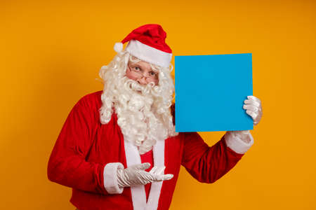 Male actor in a costume of Santa Claus holds in his hands a blue sheet of paper for records and...