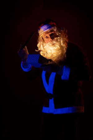Male actor dressed as Santa Claus holds a gift box in his hands, looks into it and poses on a yellow backgroundの写真素材