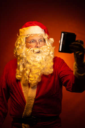 Male actor dressed as Santa Claus posing on a dark red background.の写真素材