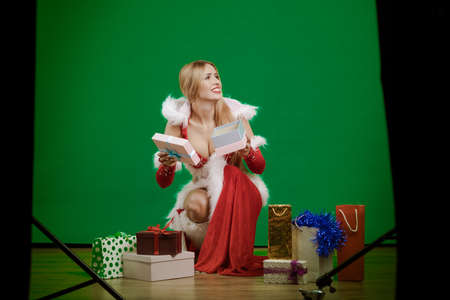 emotional young girl with long hair dressed as Santa Claus with gift boxes and packages in hands...