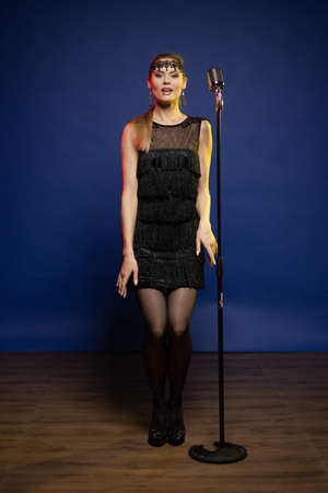 Young woman with long hair in a black dress in a retro style on a blue background. The singer sings...