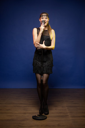 Young woman with long hair in a black dress in a retro style on a blue background. The singer sings...