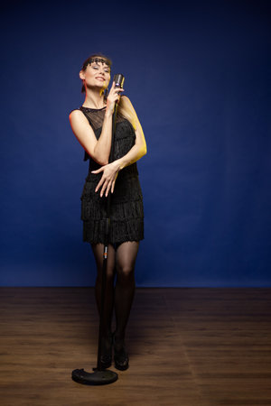 Young woman with long hair in a black dress in a retro style on a blue background. The singer sings...