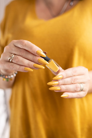 Female hand with long nails and a bottle of bright dark yellow nail polishの写真素材