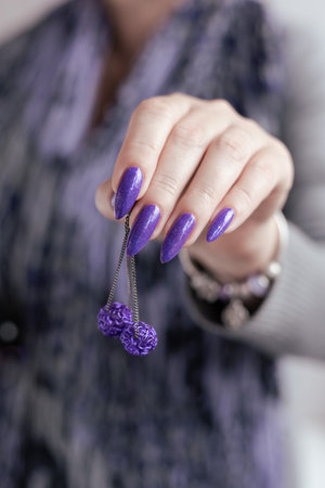 Female hand with long nails and purple lilac manicure holds a bottle of nail polishの写真素材