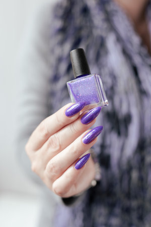 Female hand with long nails and purple lilac manicure holds a bottle of nail polish