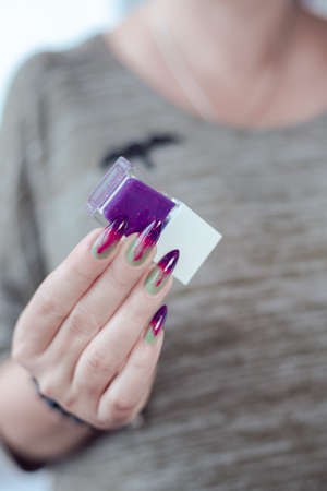 Female hands with long green and purple nails and a bottle of nail polishの写真素材