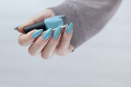 Female hand with long nails and light blue manicure with bottles of nail polish