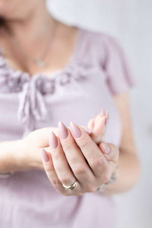 Woman hand with long nails manicure and light pink bottle with nail polish