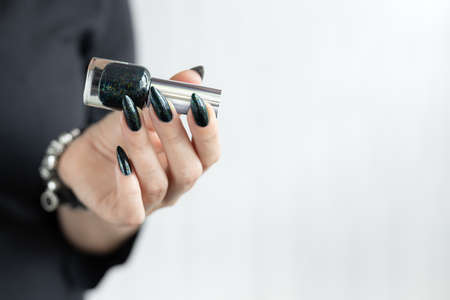 Female hand with long nails and black manicure holds a bottle of nail polish