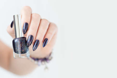 Female hand with purple long nails and nail polish bottle