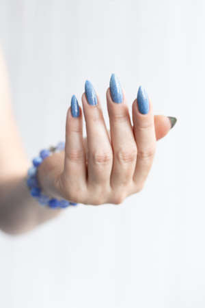 Female hand with long nails and light blue manicure with bottles of nail polishの写真素材