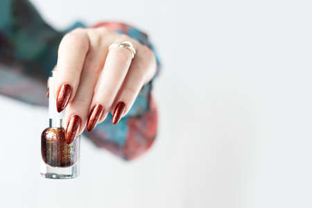 Female hand with long nails and golden brown maroon, manicure holds a bottle of nail polishの写真素材