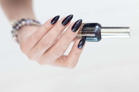 Female hand with long nails and black manicure holds a bottle of nail polishの写真素材