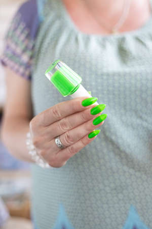 Female hand with long nails and neon green manicure with bottles of nail polishの写真素材