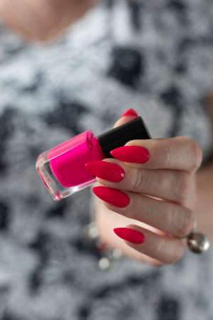 Female hand with long nails and a bottle bright neon pink red color nail polish