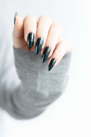 Woman's hands with long nails and dark and black manicure with bottles of nail polishの写真素材