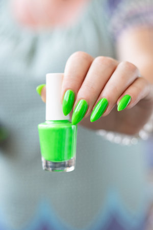 Female hand with long nails and neon green manicure with bottles of nail polishの写真素材