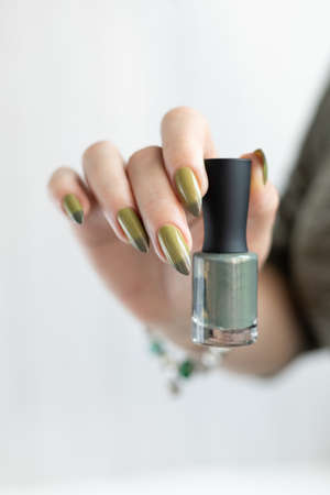 Woman's hand with long nails and light and dark green manicure with bottles of nail polishの写真素材