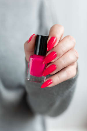Female hand with long nails and a bottle bright neon pink red color nail polishの写真素材